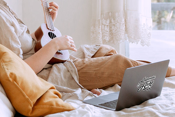 Frau lernt Ukulele-Spielen mit Laptop auf dem Bett 
