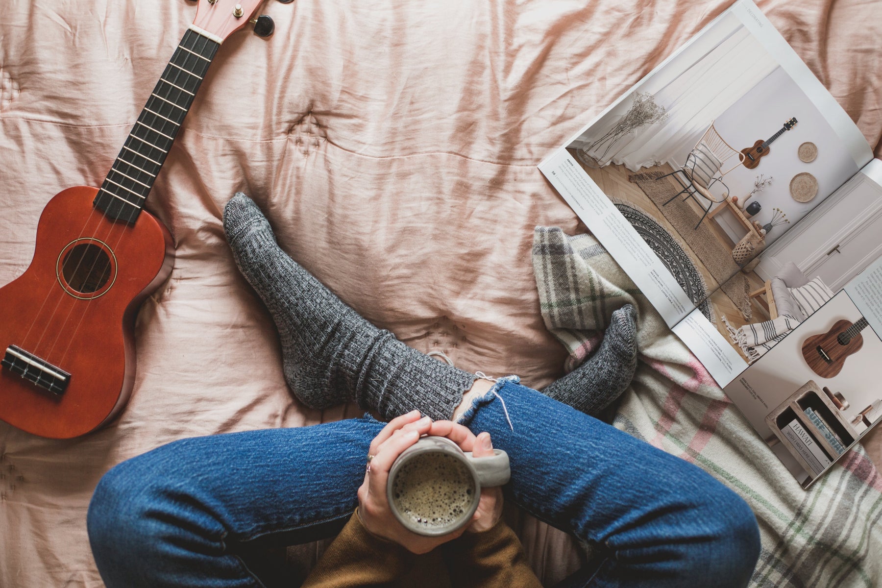 Gekreuzte Beine und warmes Getränk mit Ukulele und Magazin auf dem Bett 