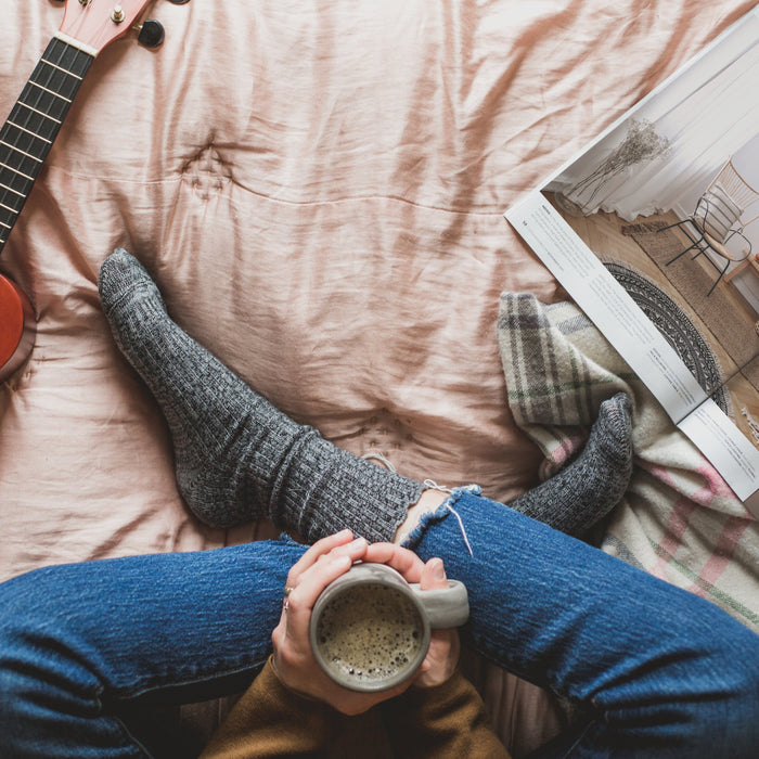 Gekreuzte Beine und warmes Getränk mit Ukulele und Magazin auf dem Bett 