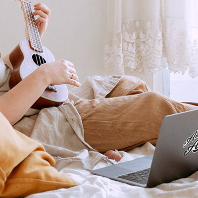 Frau lernt Ukulele-Spielen mit Laptop auf dem Bett 