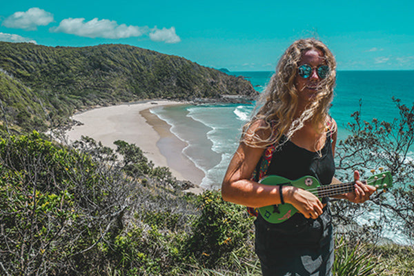 Junge Frau spielt Ukulele vor Küste und Meer